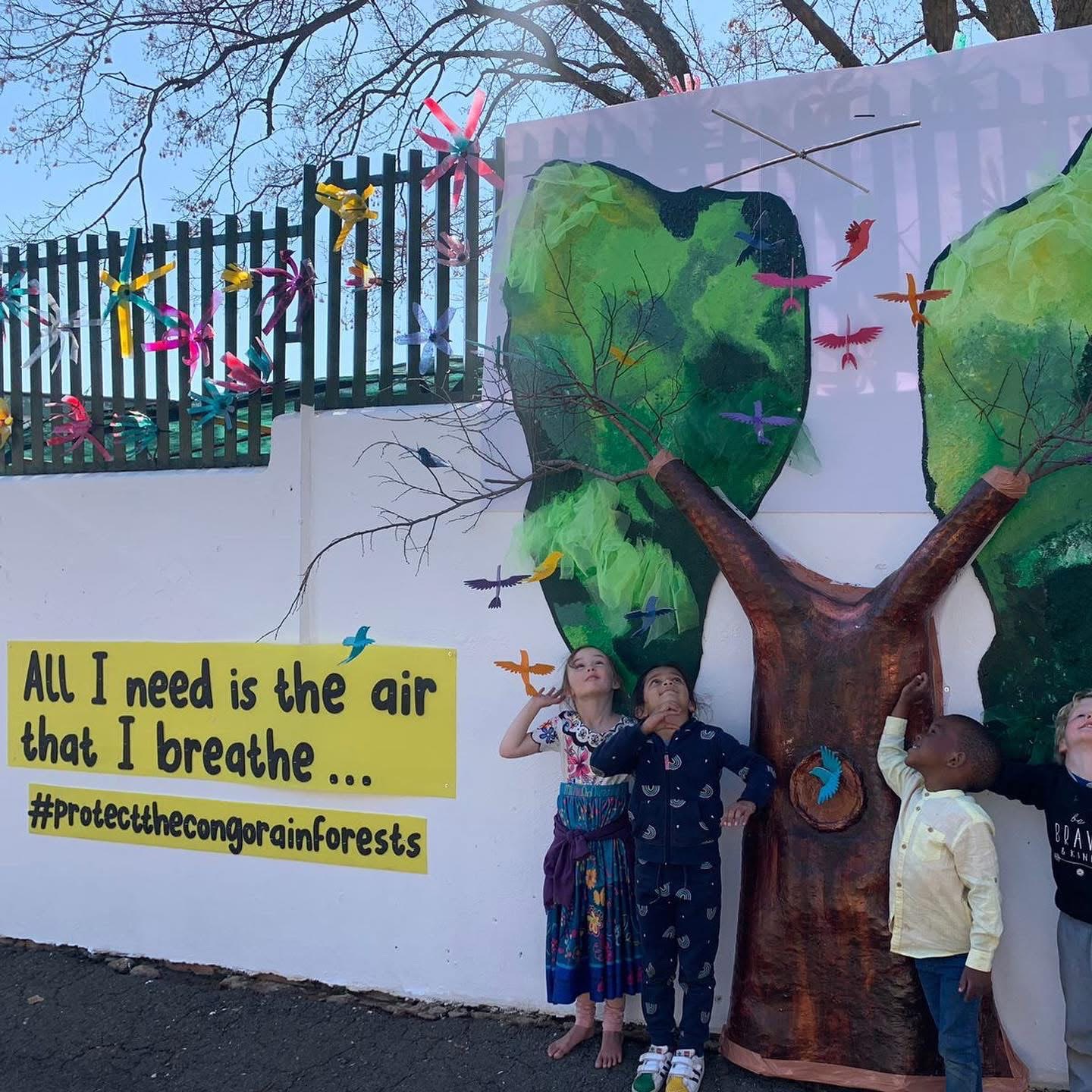 All I need is the air that I breathe rainforest mural, with children standing beside the painted tree